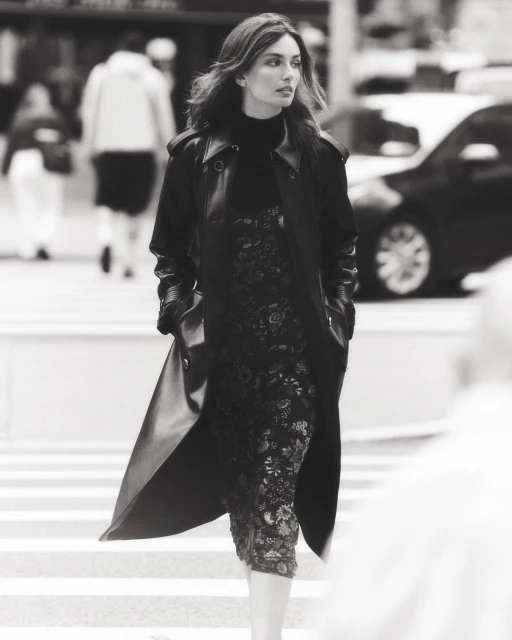Fashionable adult female walking across a crosswalk in a city street, wearing a stylish black coat and dress.