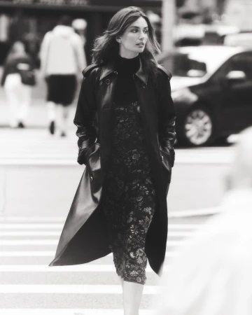 Fashionable adult female walking across a crosswalk in a city street, wearing a stylish black coat and dress.