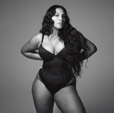Portrait of an adult woman with long dark wavy hair in a black lacy bodysuit against a grey background, fashion and beauty shot.