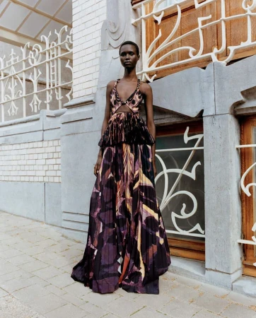 Fashion model in a long, patterned dress poses outdoors against an architectural backdrop, showcasing the garment's design and style.