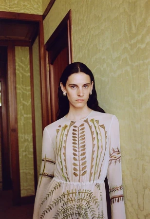 Model wearing a patterned dress standing against a textured green wall in an interior hallway