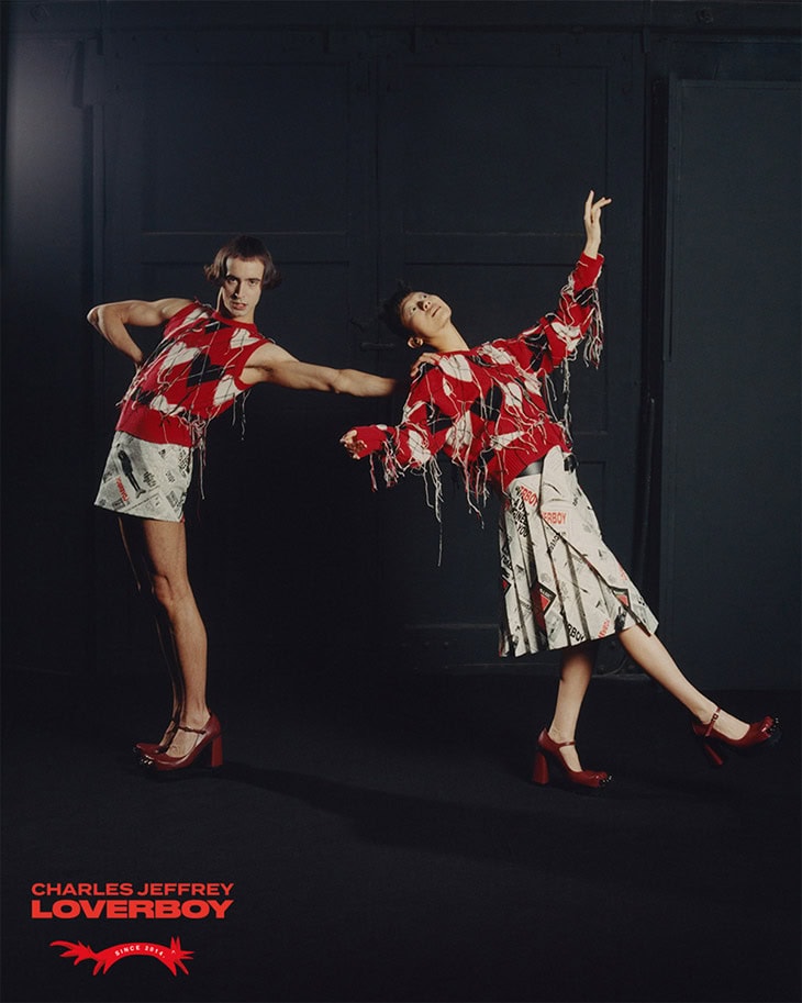 Two models strike dynamic poses in coordinating red and white outfits against a dark backdrop, showcasing avant-garde fashion design.