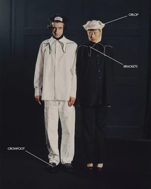 Two models standing against a dark panelled wall wearing contrasting white and black outfits by Charles Jeffrey Loverboy