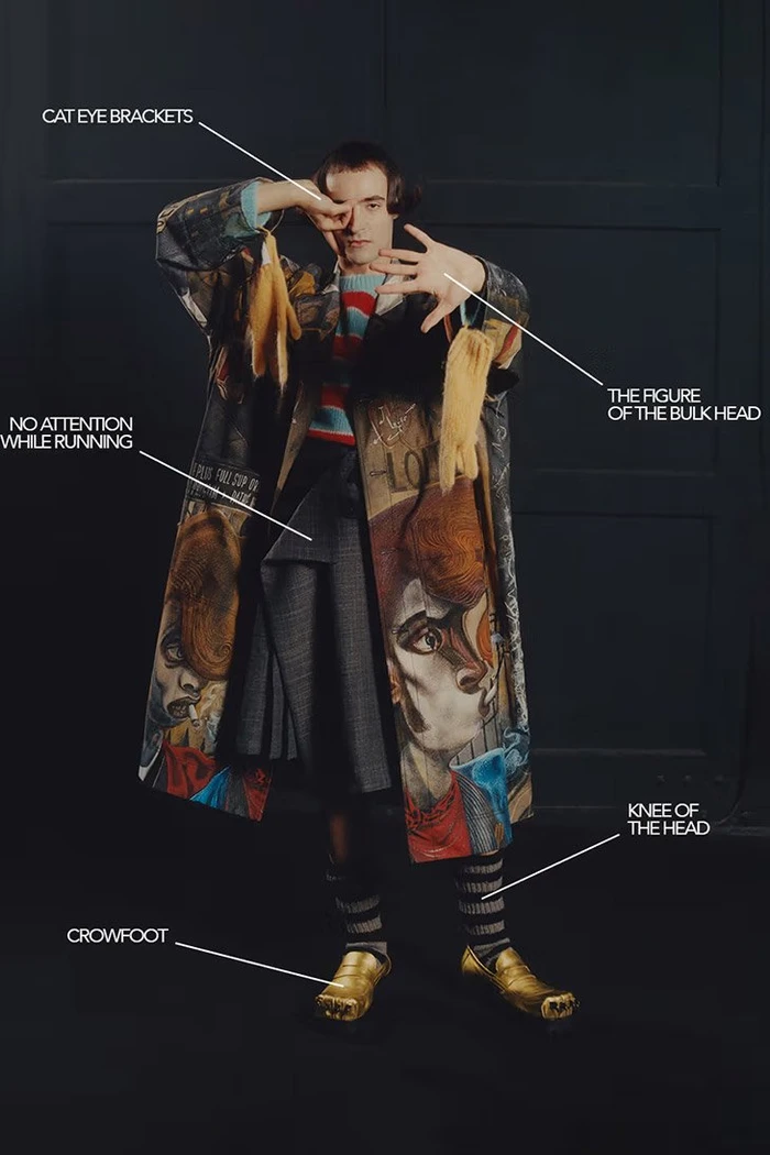 Model in printed coat with striped sweater and gold shoes against a dark background for Charles Jeffrey Loverboy