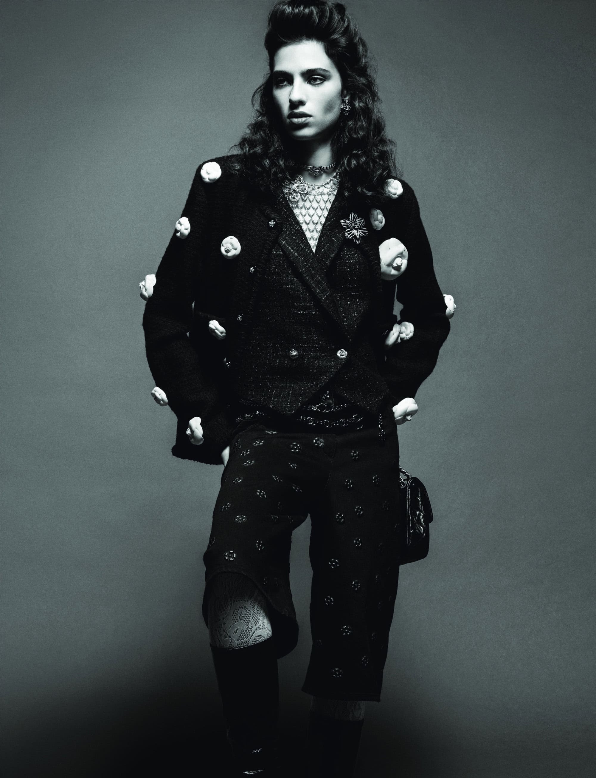 Monochromatic fashion portrait of a stylish adult female model in a patterned suit jacket and culottes posing against a grey backdrop.