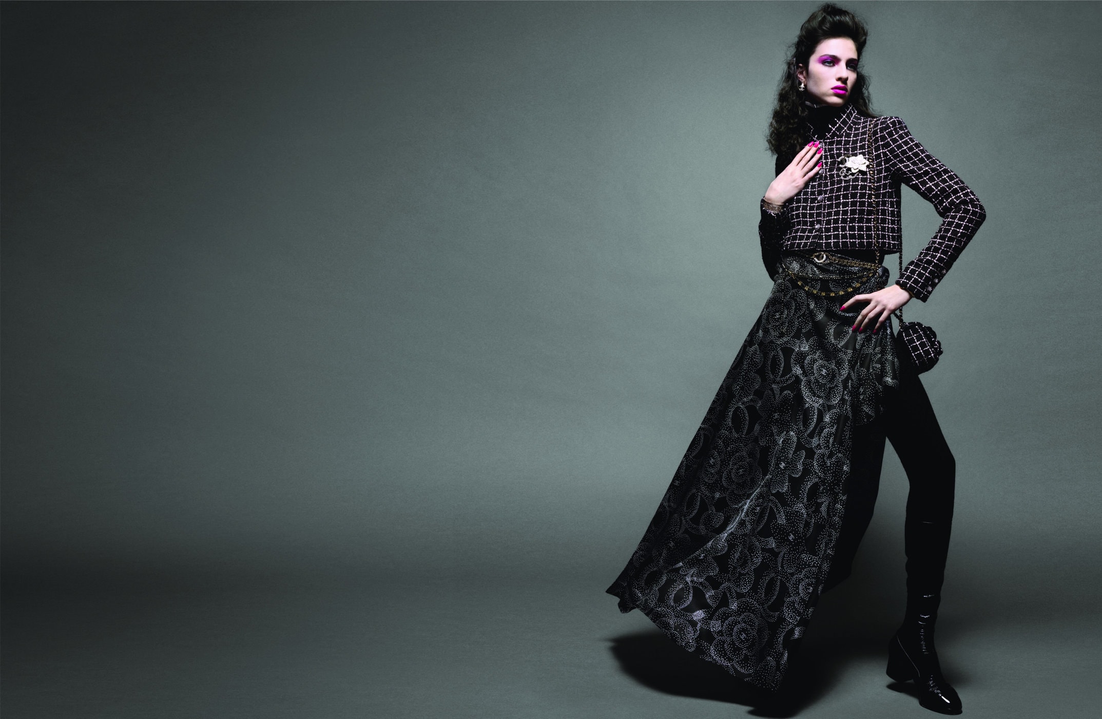 A stylish fashion model in a black and white patterned ensemble poses in a studio setting with a gray background, showcasing high-fashion.