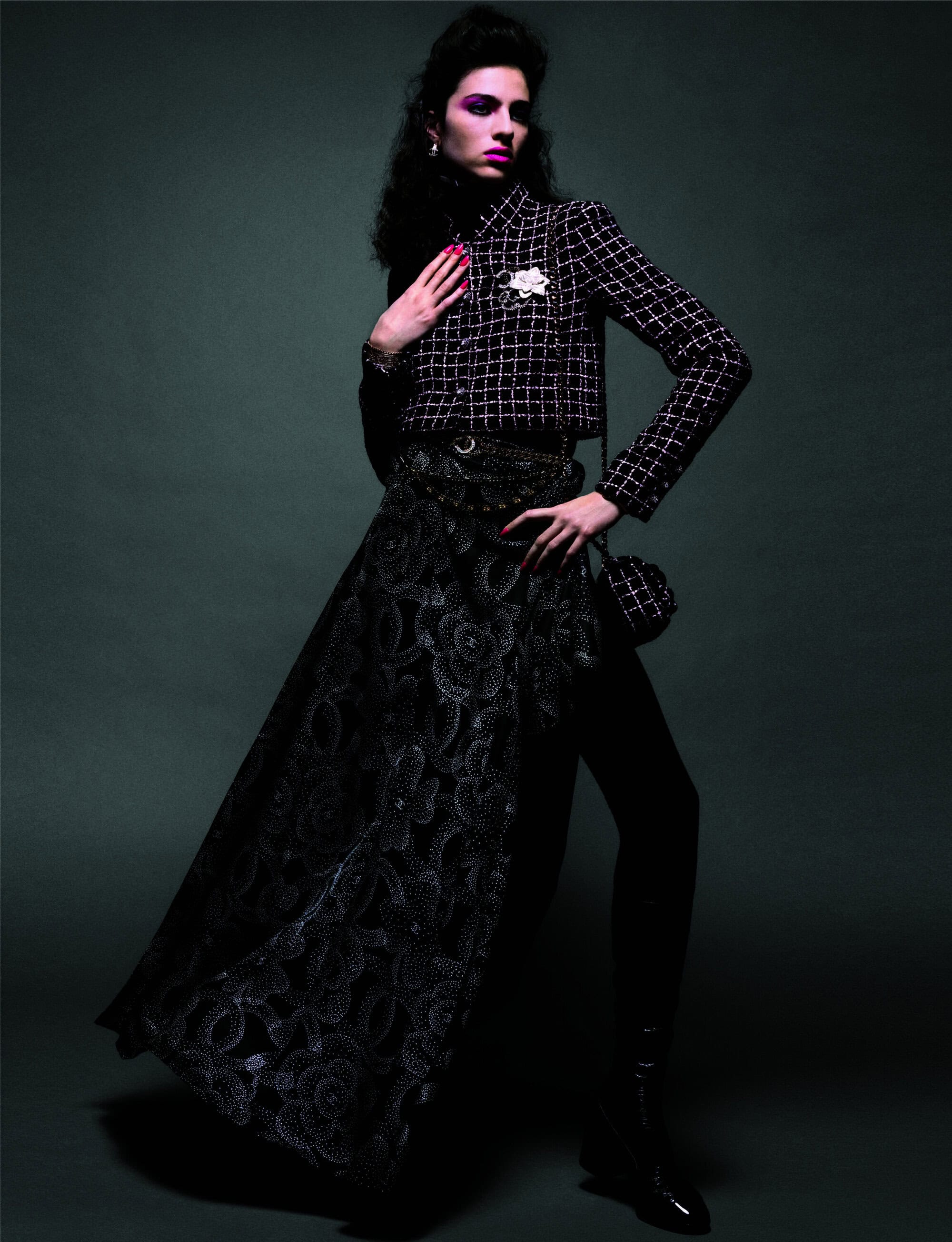 A woman in a black-and-white checkered jacket and long black skirt poses in a studio with low-key lighting and a dark-green background.