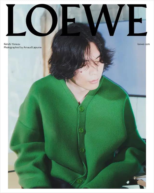 Adult male in a green cardigan sweater with black hair, featured on a magazine cover with 'LOEWE' text, casual indoor setting.