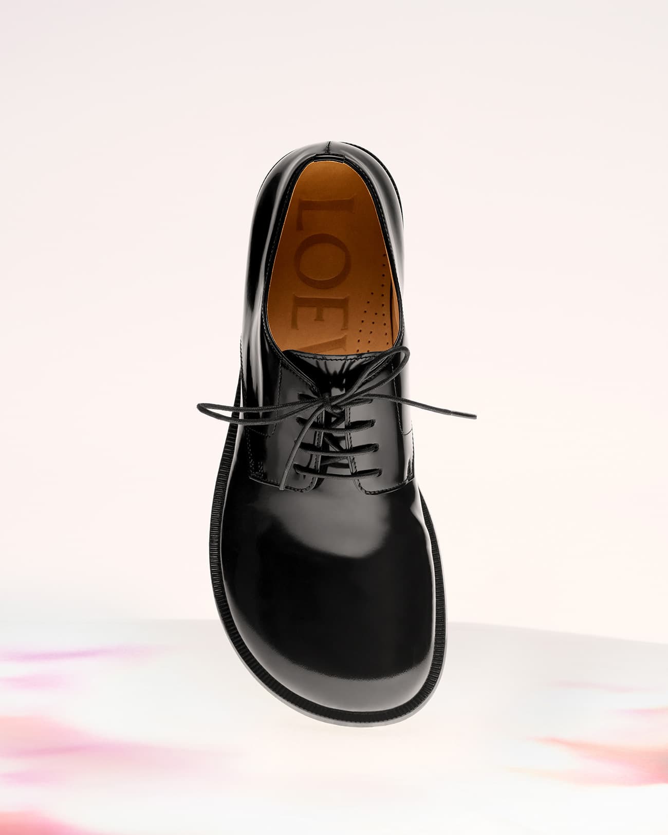 Elevated view of a single black leather Loewe dress shoe with laces, floating in a studio setting against a soft, light background.
