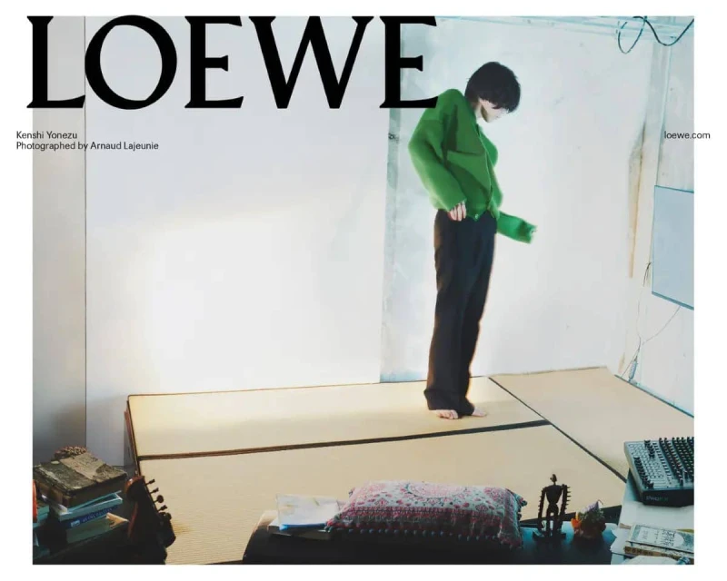 Loewe fashion editorial featuring a barefoot adult male in a green sweater and black pants standing in an indoor setting.