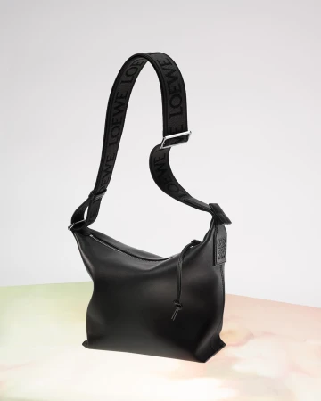 Studio shot of a black leather Loewe handbag with a patterned shoulder strap on a gradient background, showcasing its sleek design.