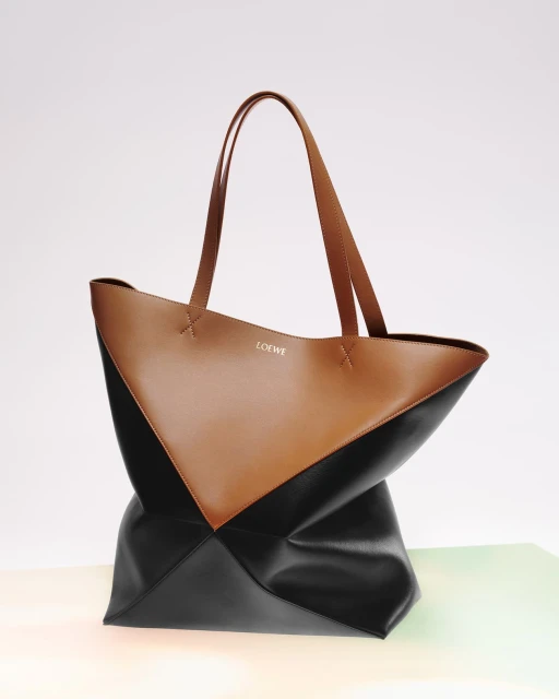 Tan and black leather Loewe tote bag with top handles, photographed on a gradient white background in a studio setting.
