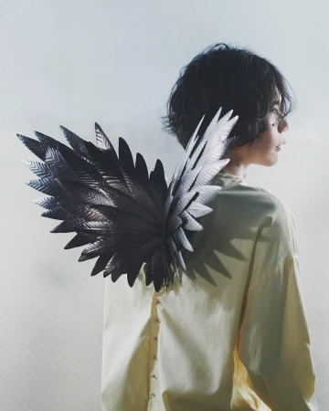Kenshi Yonezu wearing a pale yellow shirt with large sculptural black wings attached to the back for a Loewe ad campaign.