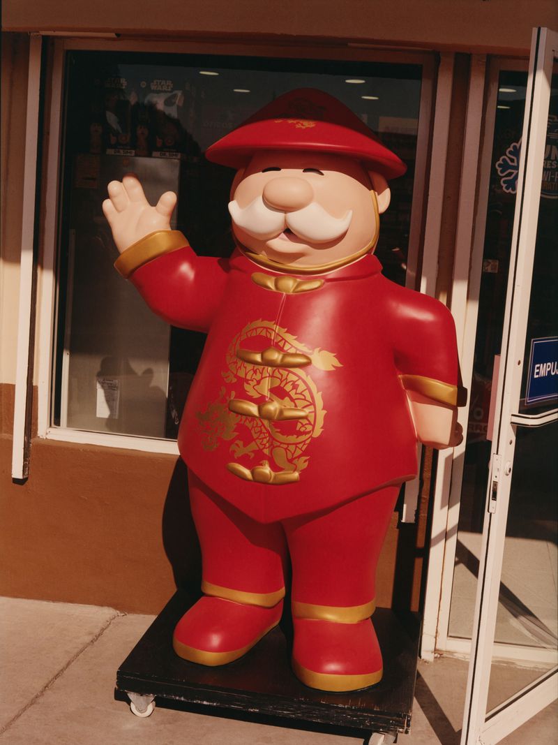 Outdoor view of a decorative figure in a red and gold outfit with a hat, standing near a door with windows.