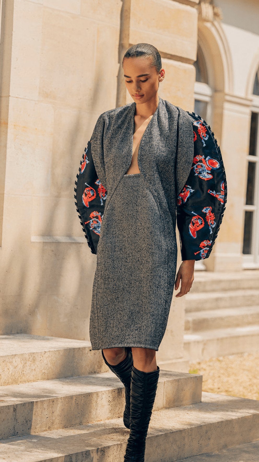 Woman in a grey tweed dress with floral puff sleeves walks down stone steps in an outdoor setting, fashion photoshoot, full shot.