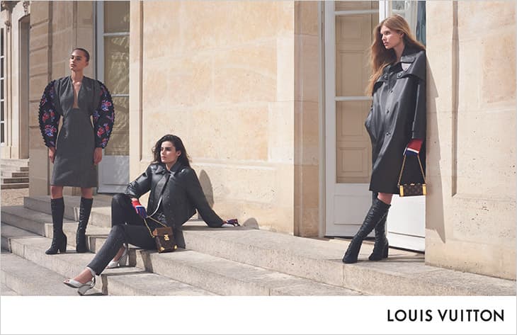 Three fashion models pose outside a building, showcasing clothing and accessories. Two wear knee-high boots, one is seated on stairs.