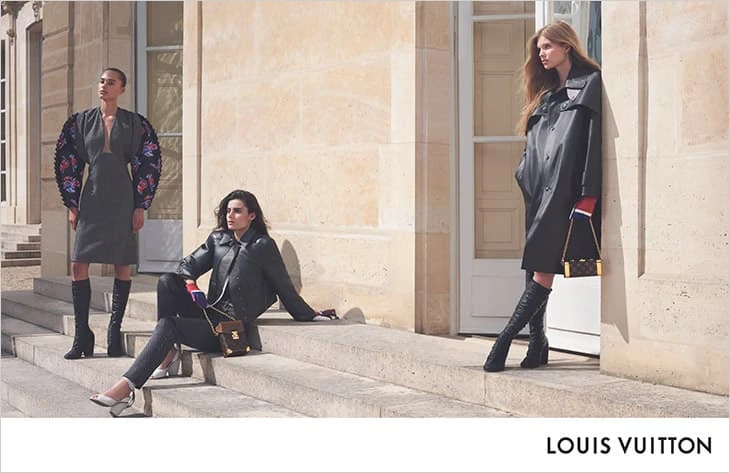 Three fashion models pose outside a building, showcasing clothing and accessories. Two wear knee-high boots, one is seated on stairs.