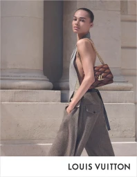 Model in grey sleeveless top and trousers carrying a quilted brown chain-strap handbag against neoclassical columns