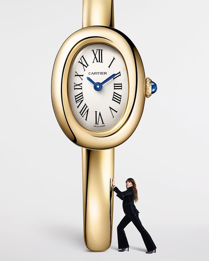Woman pushes a giant golden Cartier watch in a studio setting, highlighting the watch's design and her interaction with the oversized timepiece.