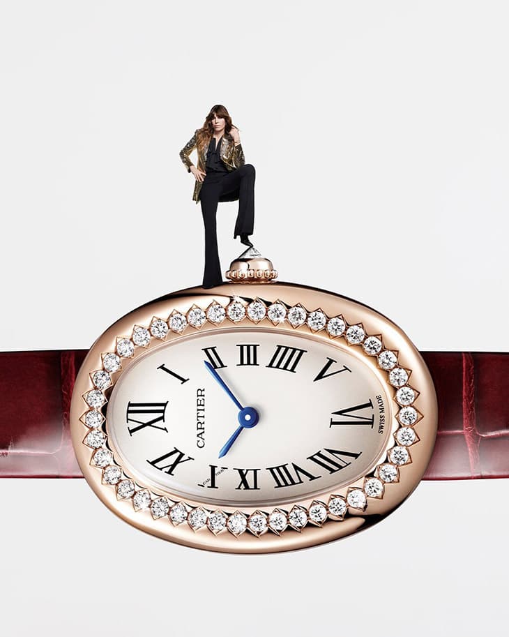 Wristwatch with a gold case, diamond bezel, and a woman in a gold blazer and black pants standing atop the watch winder.