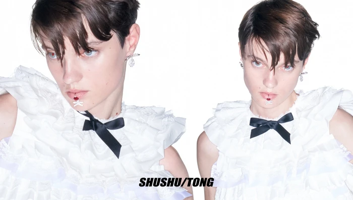 Model Tanya Churbanova wearing a white ruffled top with a black bow and cherry lip jewelry against a white background for Shushu/Tong.