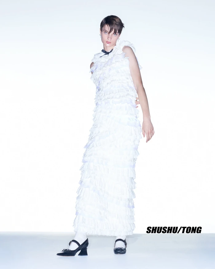 Model in ruffled white dress and black Mary Jane shoes against a white backdrop for Shushu/Tong Fall 2023