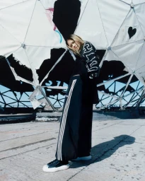 Model posing in black oversized Y-3 track pants and long-sleeve top under a torn geodesic dome on a Berlin rooftop.