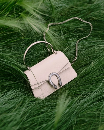 Elegant cream-colored leather handbag with silver chain and jeweled clasp displayed on a vibrant bed of green grass.