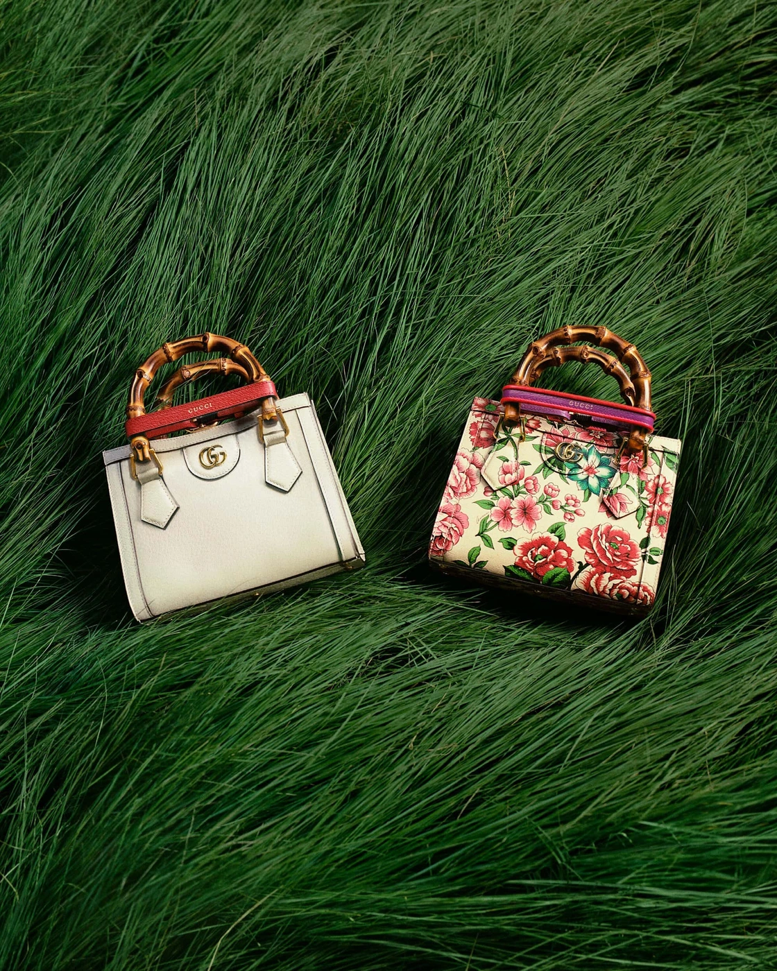 Two Gucci bamboo handle mini tote bags resting among lush green tall grass viewed from above.