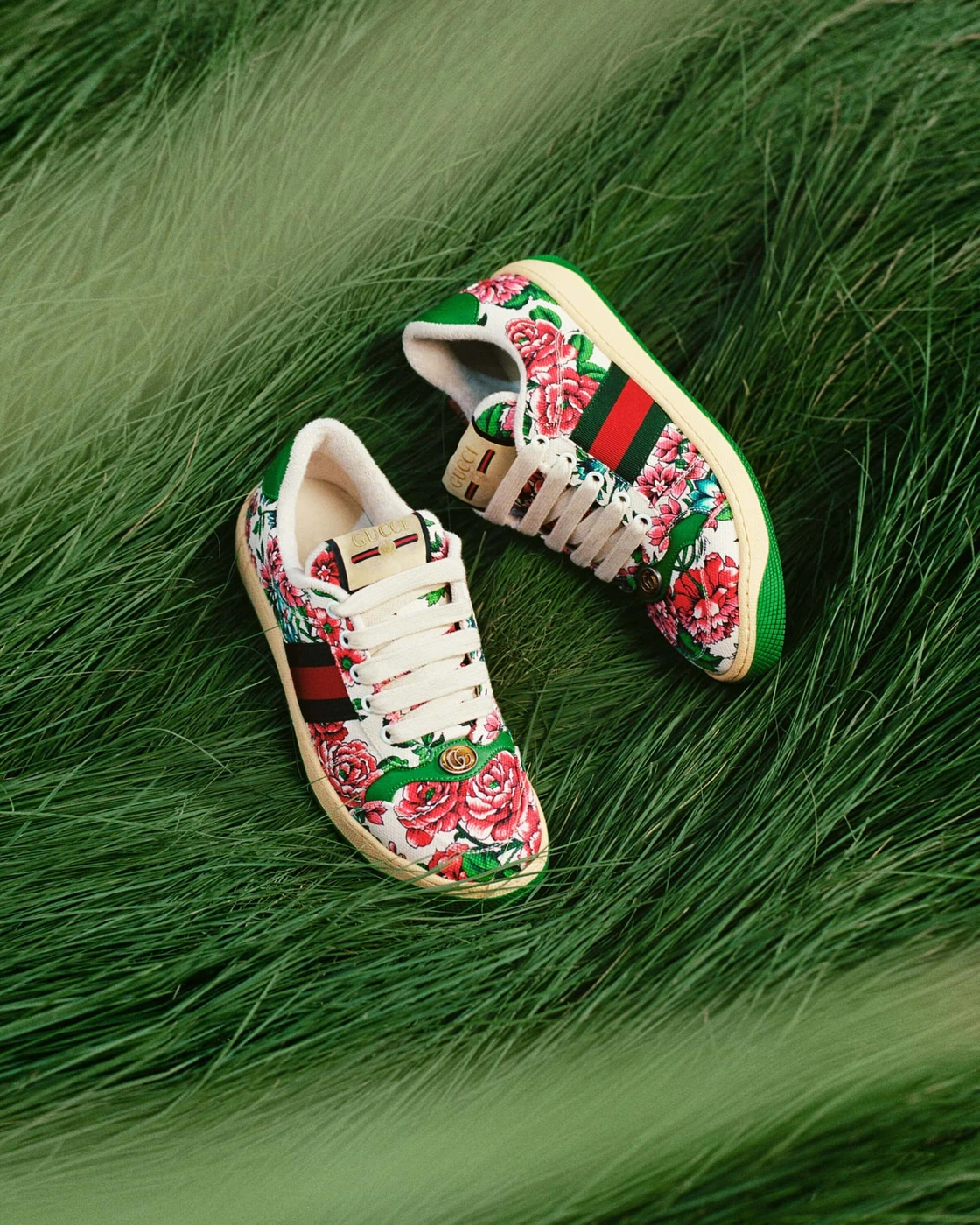 A pair of Gucci floral-print low-top sneakers nestled among lush, tall blades of green grass.