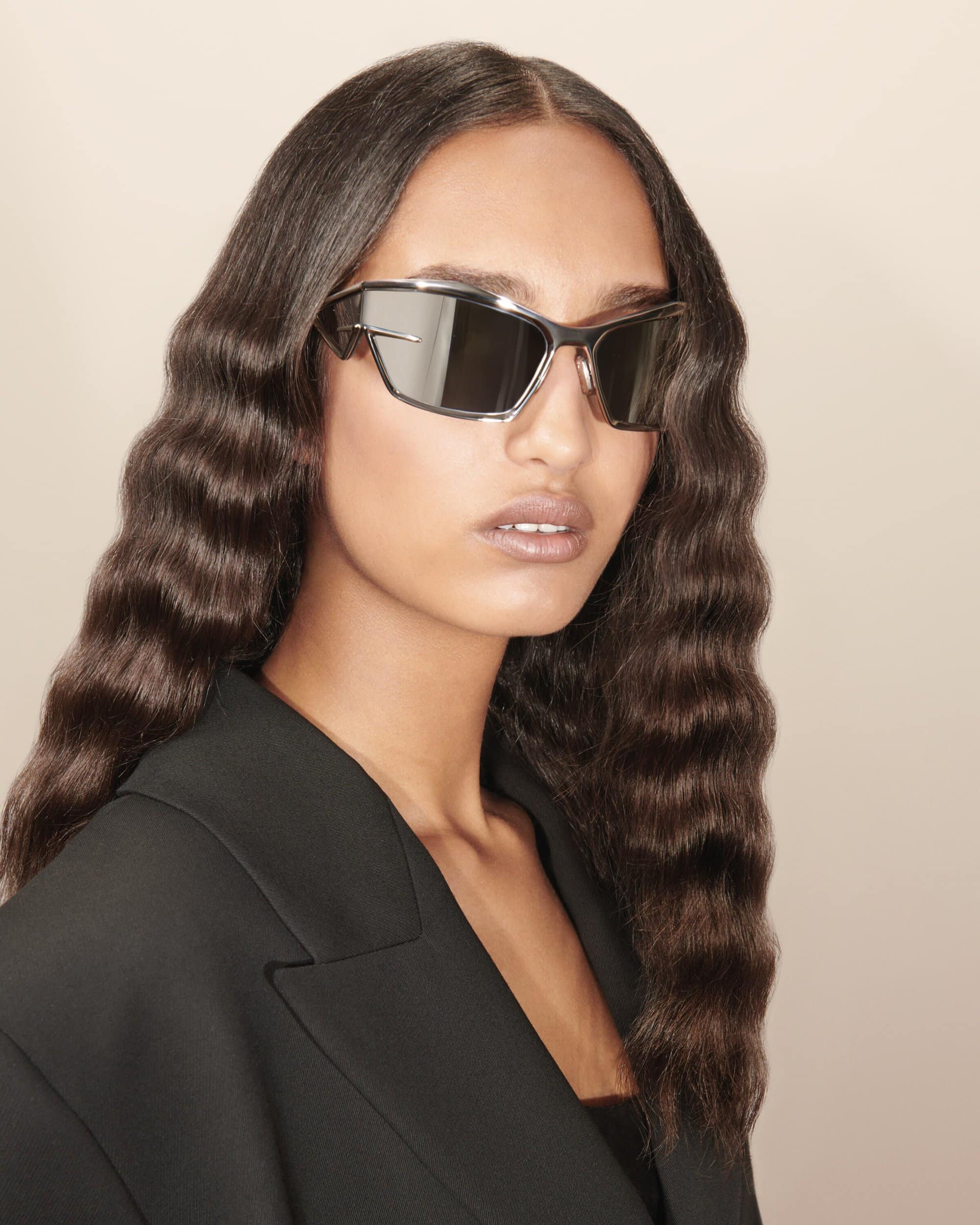 Portrait of a stylish woman wearing futuristic sunglasses and a black blazer, showcasing modern fashion and eyewear trends.