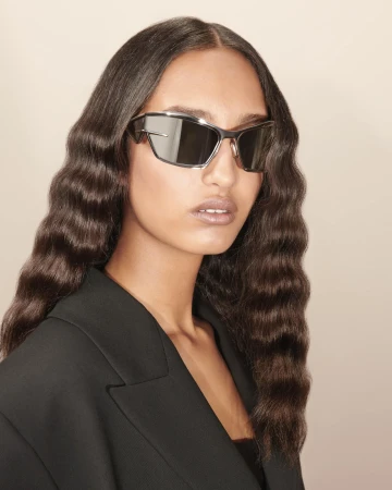 Portrait of a stylish woman wearing futuristic sunglasses and a black blazer, showcasing modern fashion and eyewear trends.