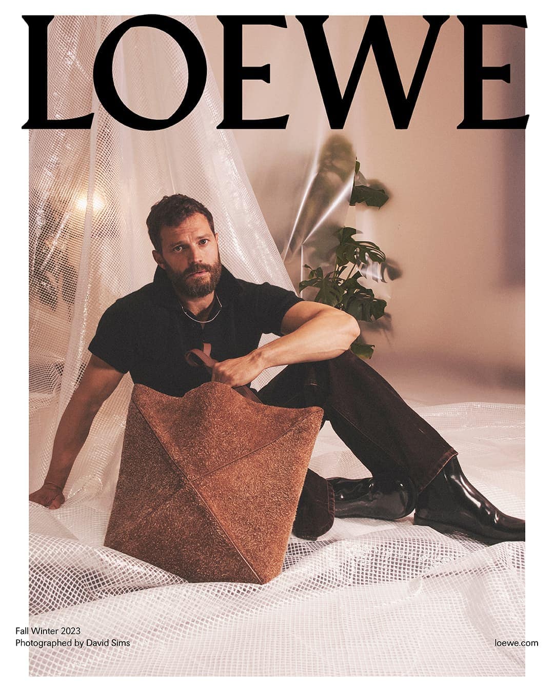 Jamie Dornan poses with a brown, textured pyramidal handbag in a studio setting for a Loewe fashion advertisement, Fall/Winter 2023.