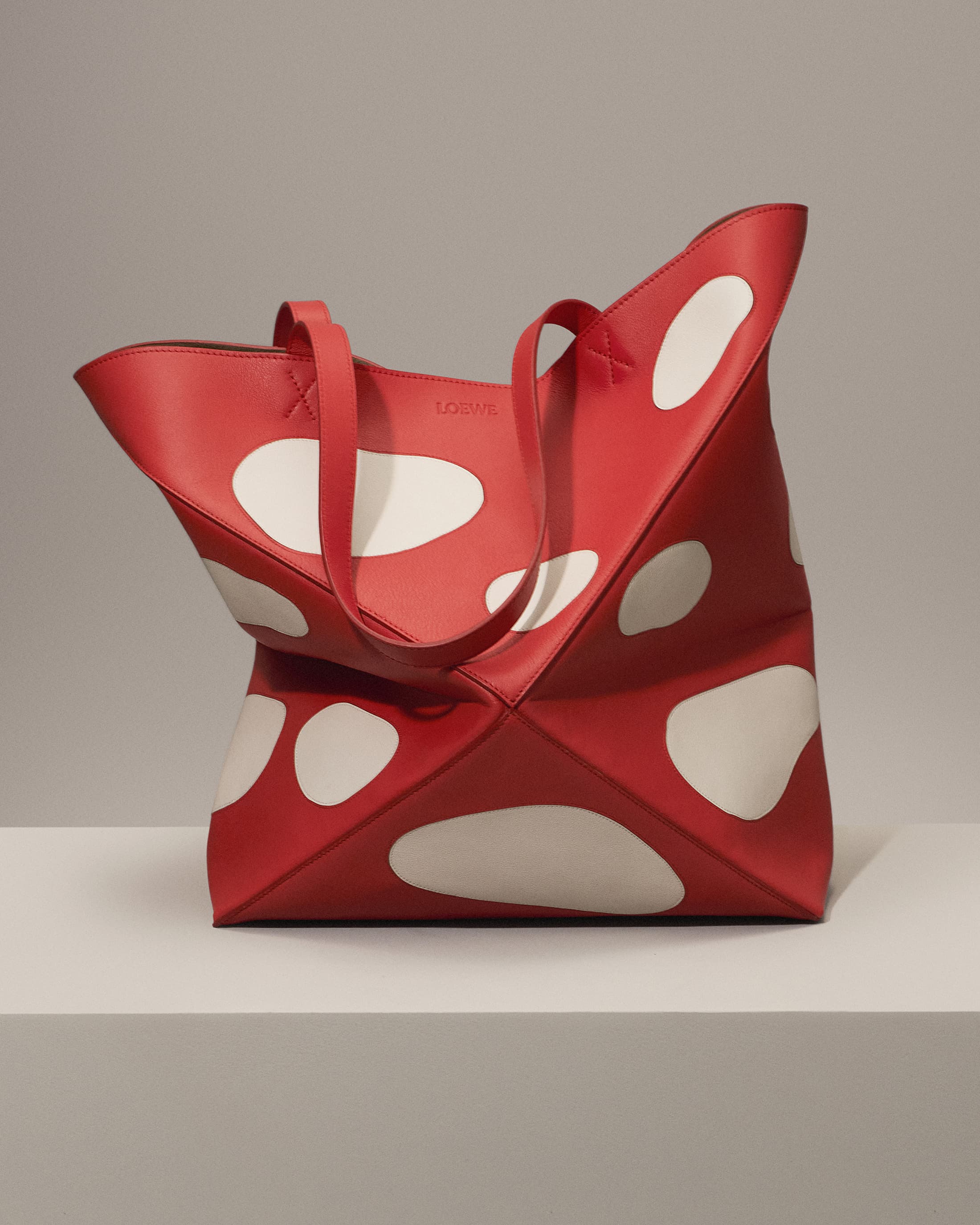 Stylish red leather tote bag with white polka dots. Modern design for fashion, shopping, or everyday use on a neutral background.