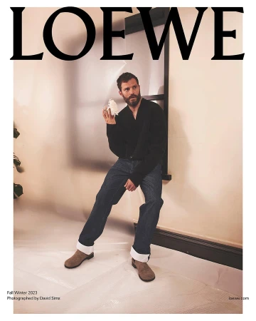 Jamie Dornan poses in Loewe Fall/Winter 2023 ad, wearing a black cardigan, jeans, and suede boots, with the Loewe logo.
