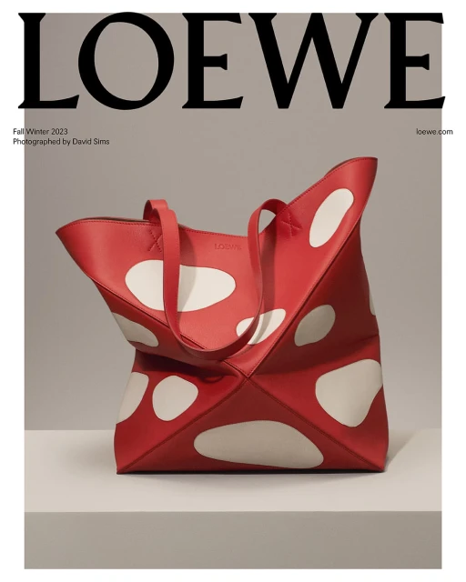 Red Loewe tote bag with white polka dots on a light gray shelf and background, featuring the Loewe logo at the top.