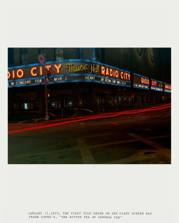 Vintage shot of Radio City Music Hall's facade at night with glowing neon signs and blurred streaks of red lights in the foreground.
