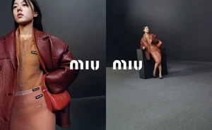 Model wearing a burgundy leather jacket and sheer skirt with a red handbag in a Miu Miu campaign shot against a grey studio backdrop