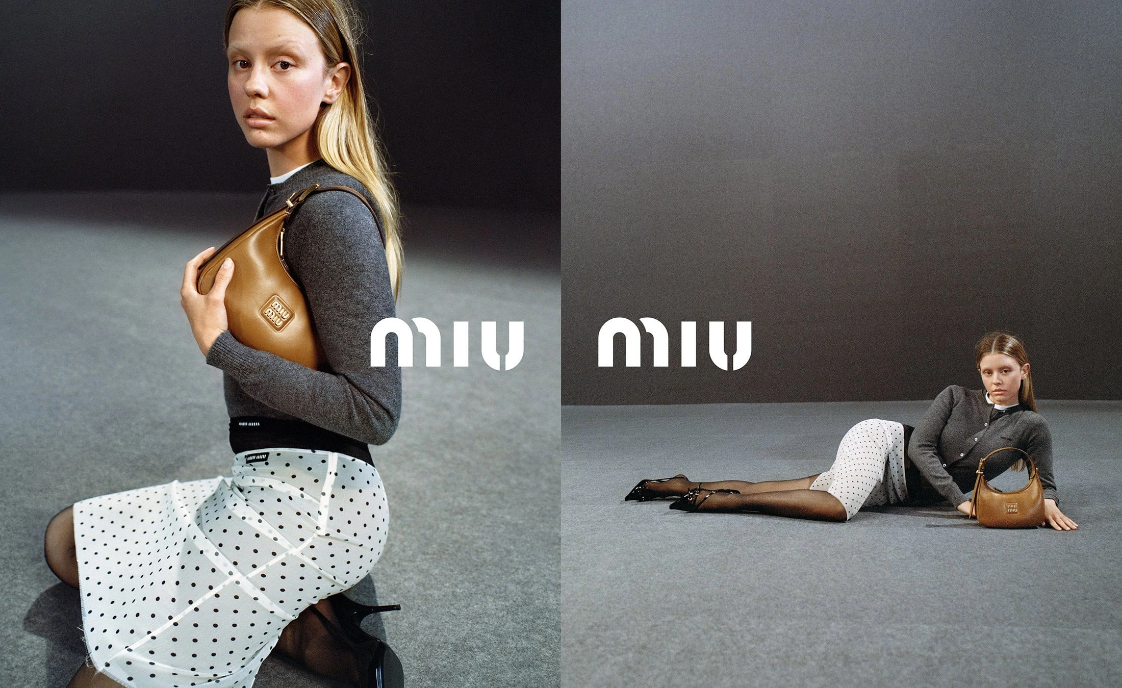 Mia Goth holding a brown leather bag wearing a grey cardigan and polka dot skirt against a grey seamless backdrop