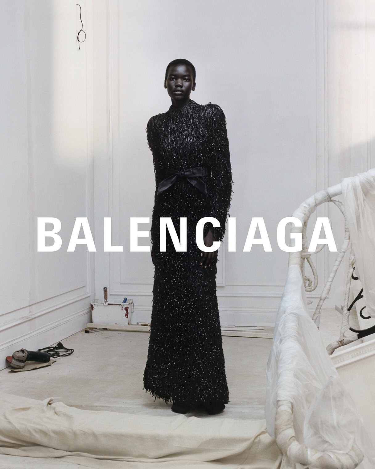 An African American fashion model poses in a studio wearing a long, black sequined gown with a black bow belt for Balenciaga.