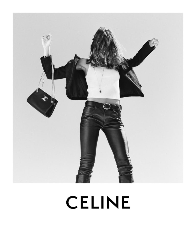 Fashion editorial shot in black and white featuring a female model in leather pants and jacket holding a handbag against a light background.