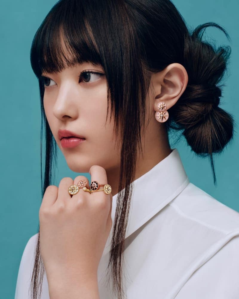 Close-up portrait of a woman wearing gold star motif rings and earrings against a solid teal background