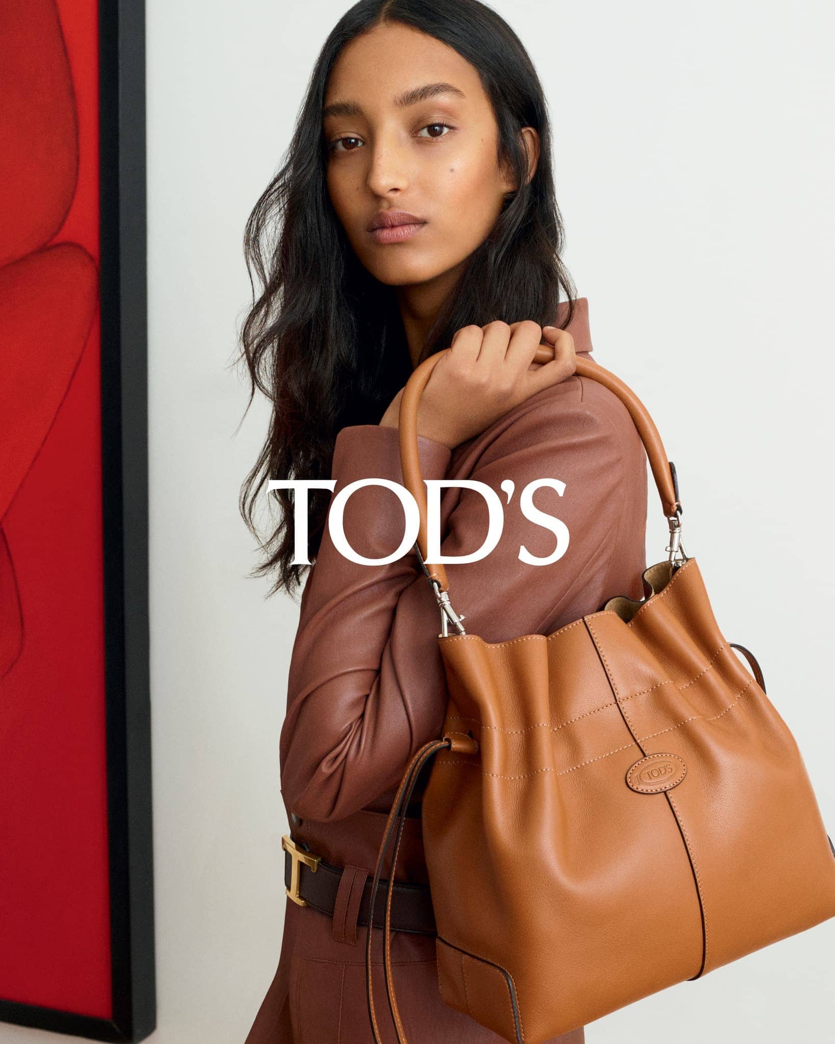 Fashion shot featuring a woman in a brown jacket and a brown leather Tod's handbag, studio setting with a red abstract painting.