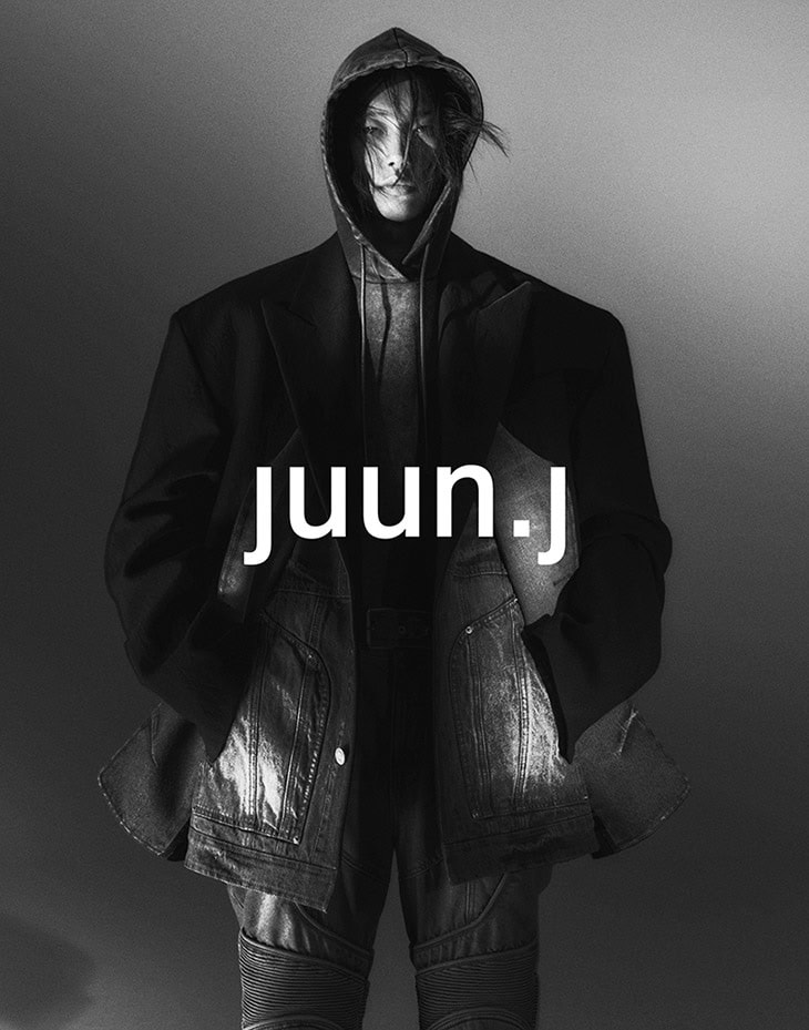 Monochrome fashion portrait of person in hooded sweatshirt, oversized jacket, and jeans, brand name 'juun.j' overlaid on center frame.