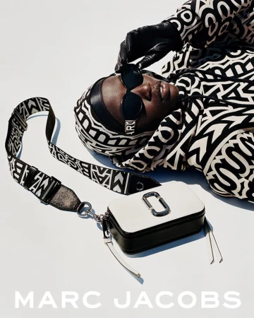 Fashion shot of an adult Black female model with sunglasses, headscarf, and a white Marc Jacobs handbag on a light backdrop.