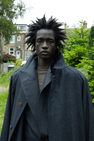 Portrait of a black man wearing a dark grey wool coat outdoors against a residential building background.