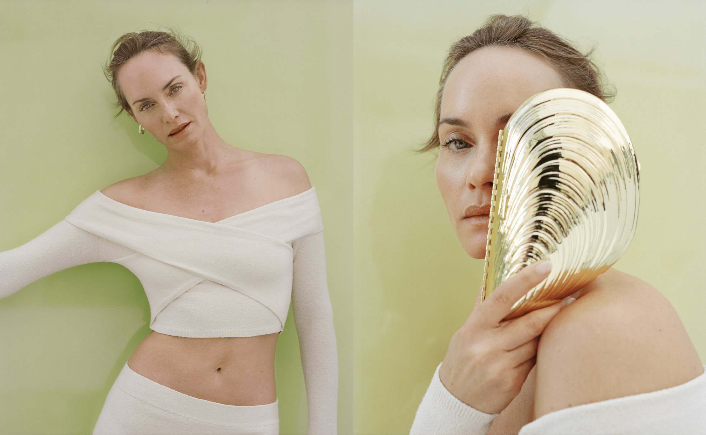 Studio shot of an adult woman in an off-the-shoulder crop top, posing with a gold seashell in front of a light green backdrop.