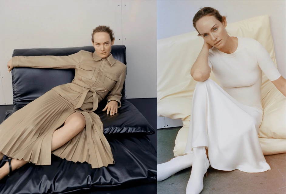 Fashion shot of a woman in a tan dress seated on a black cushion and a woman in a white dress and boots seated on a cushion.