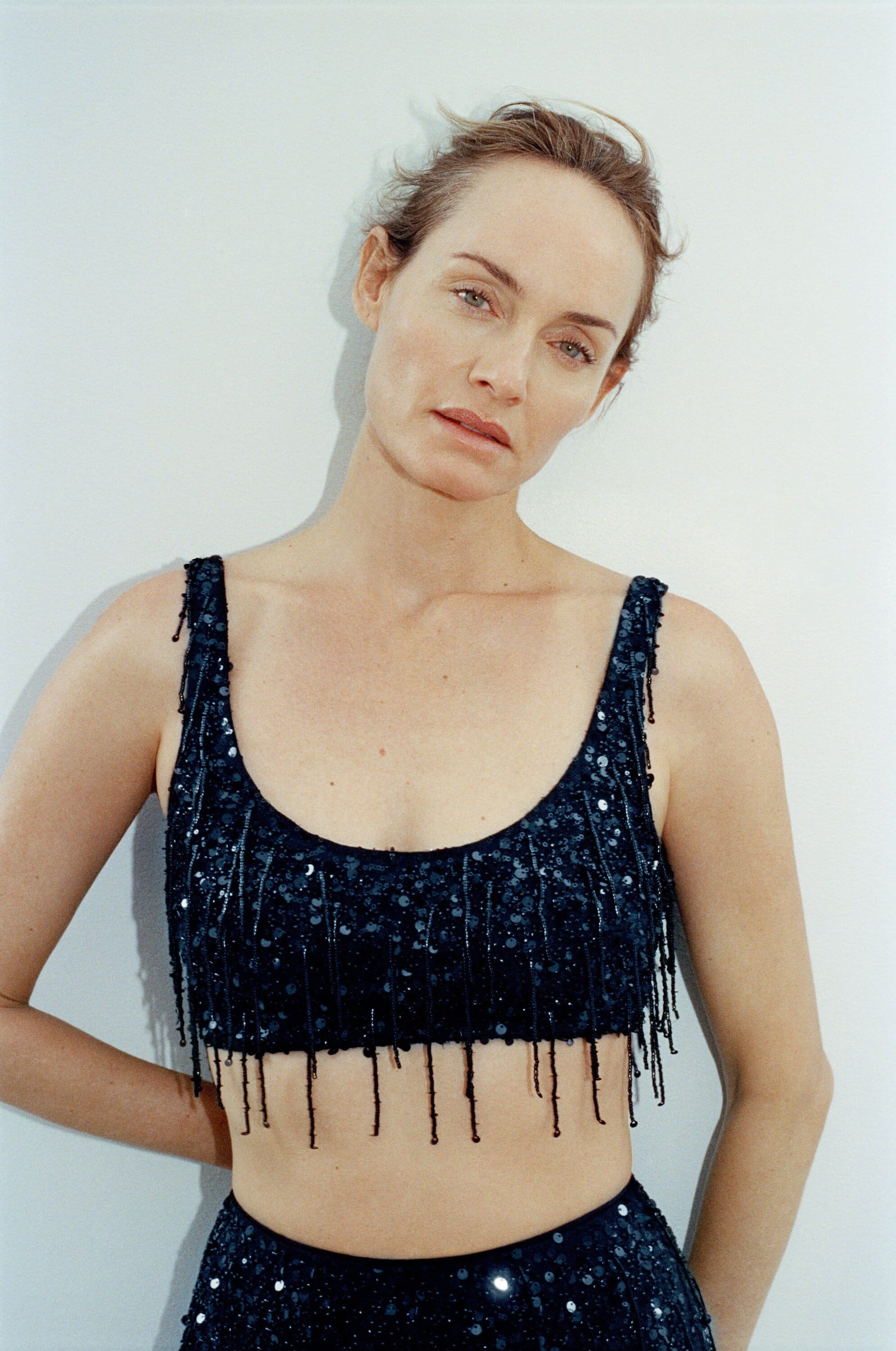 Woman posing in a blue sequined two-piece outfit against a pale wall, bathed in soft lighting. Fashion shot, close-up view.