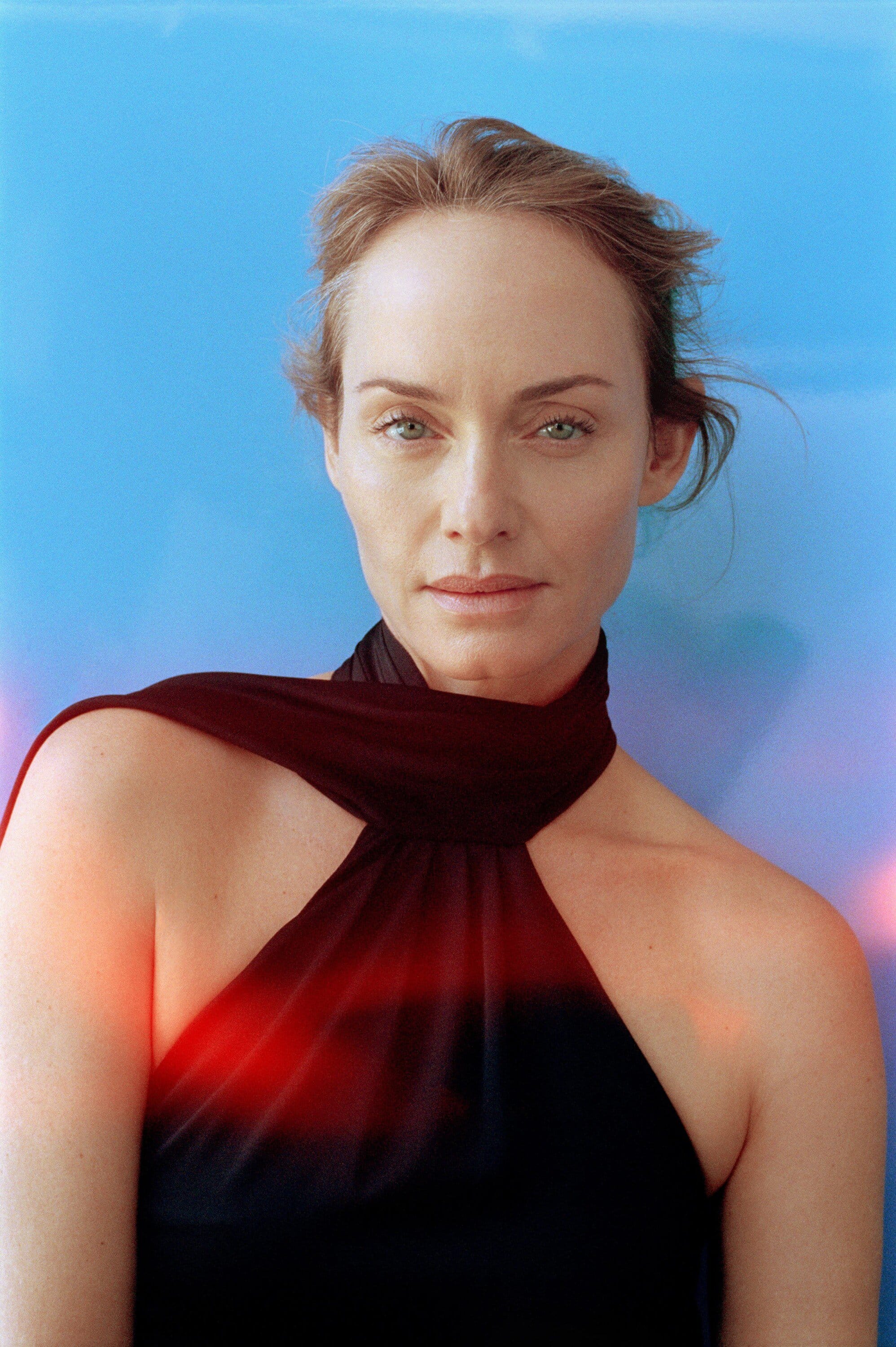 Portrait of a fair-skinned adult woman with shoulder-length hair against a graduated blue background, wearing a sleeveless black dress.